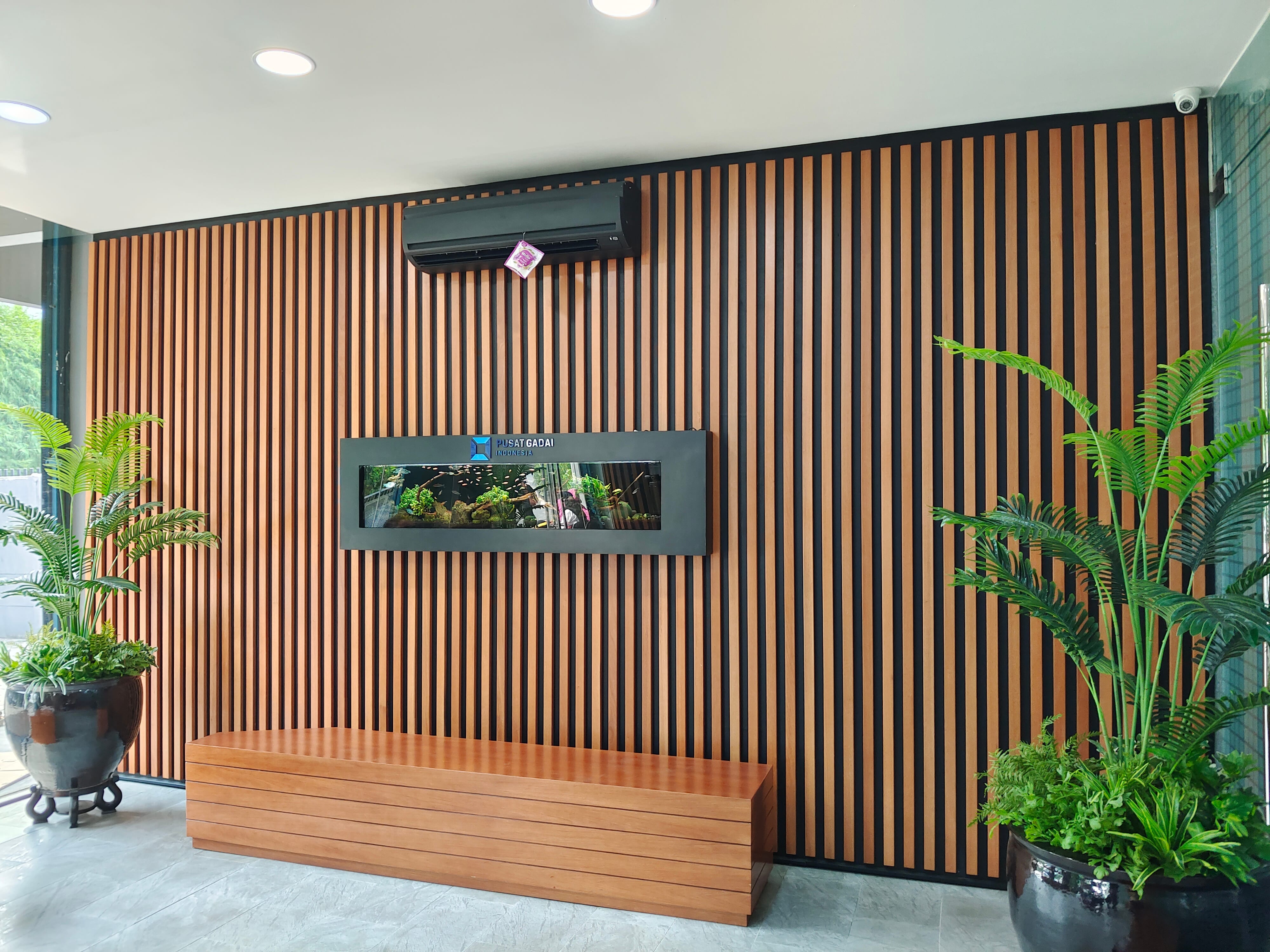 Full-height vertical slat wall cladding with integrated aquarium and solid wood bench seat at Pusat Gadai by Reywood